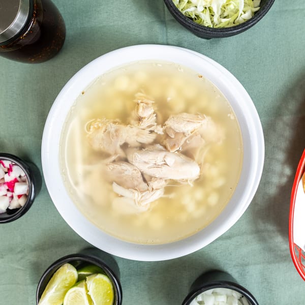 Chicken pozole soup with hominy, shredded chicken, and sides of radishes, limes, cabbage, and chips.