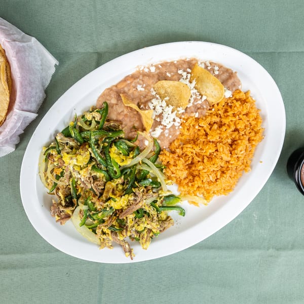 Plate of scrambled eggs with peppers and meat, rice, refried beans, tortillas, and salsa.