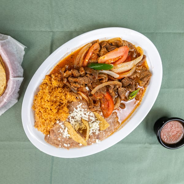 Beef fajitas with sautéed onions, tomatoes, rice, refried beans, tortillas, and salsa on a green tablecloth.