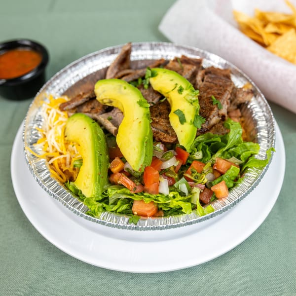 Foil container with steak, avocado, lettuce, pico de gallo, and cheese, served with salsa and chips.