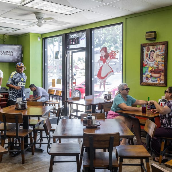 Customers dining and standing in a casual restaurant with green walls and wooden tables.