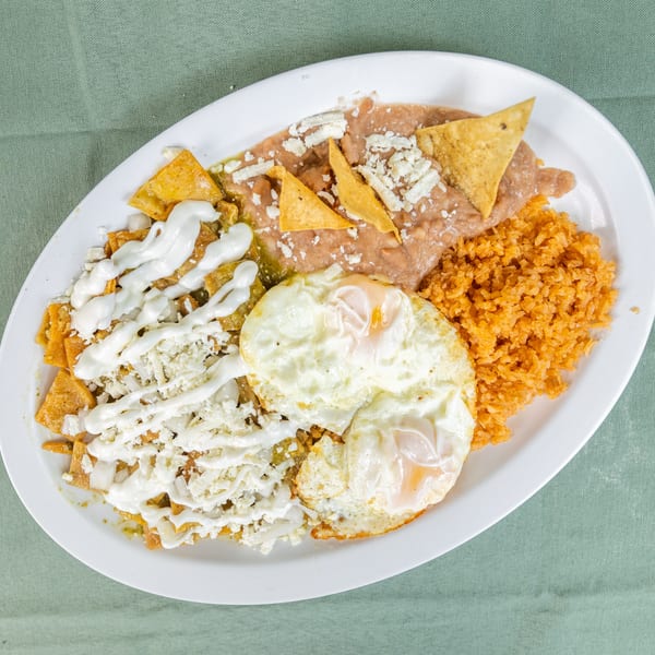 Oval plate of chilaquiles with green sauce, fried eggs, refried beans, and red rice.