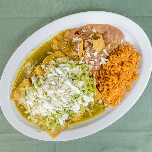 Green enchiladas topped with lettuce, cheese, and sour cream, served with refried beans and rice.