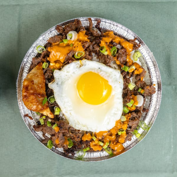 Beef and rice bowl with a fried egg, orange sauce, green onions, and a dumpling.