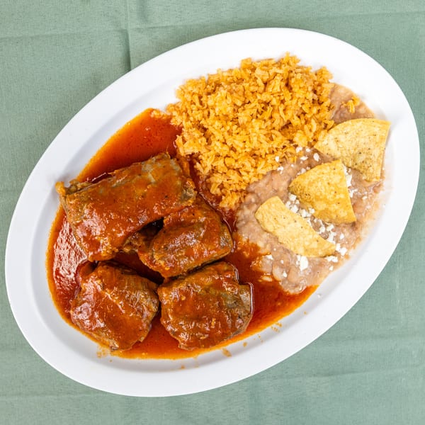 Plate of stewed meat in red sauce, Mexican rice, refried beans, and cheesy tortilla chips.